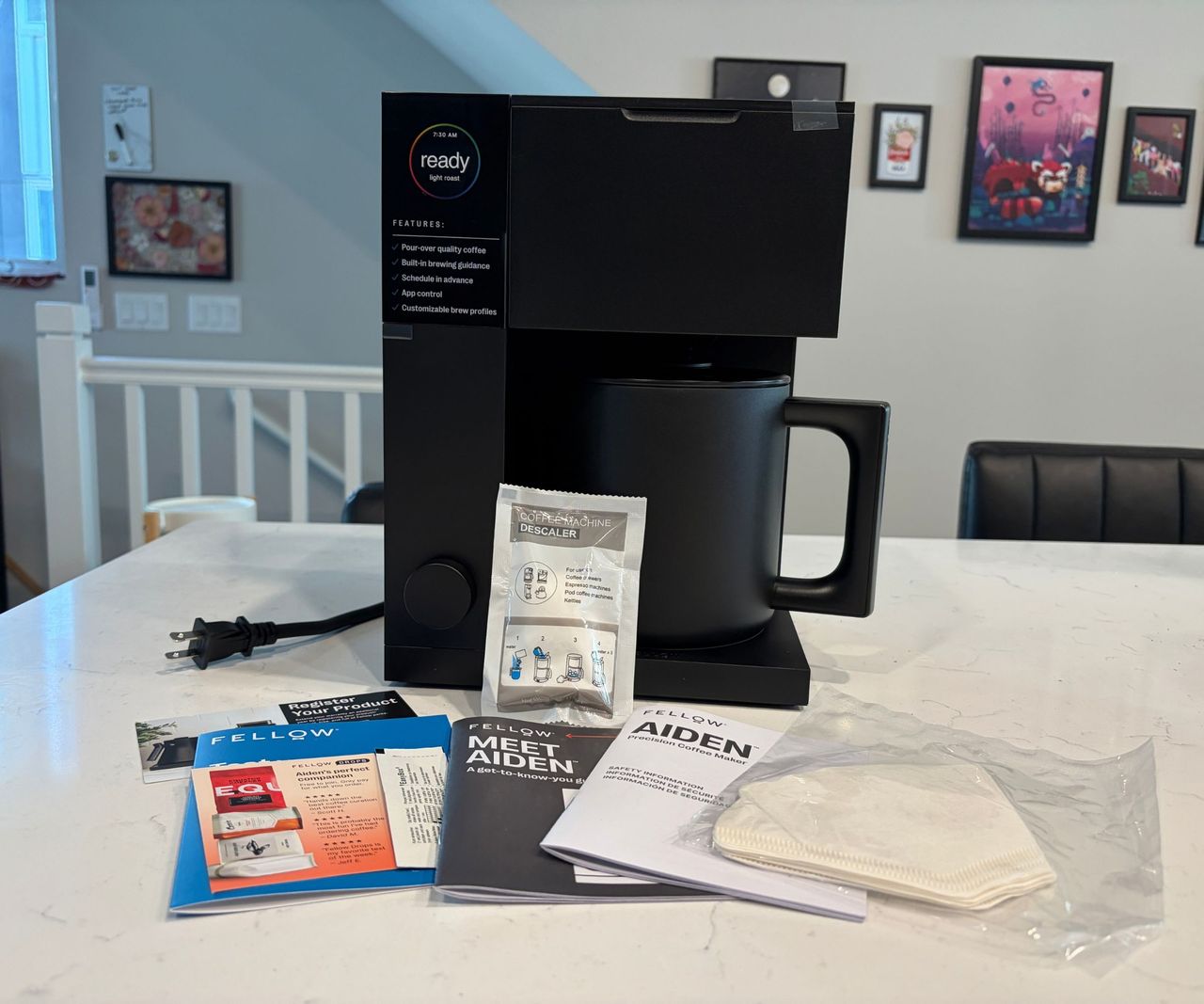 A black blocky coffee maker with an array of paper leaflets in front of it, on a white kitchen counter.