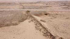We see a bird's-eye view image of the sandy and rocky desert of northern Peru. Running diagonally in the photo is a high stone wall.