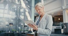 A mature businesswoman reviews her finances on a tablet while walking.