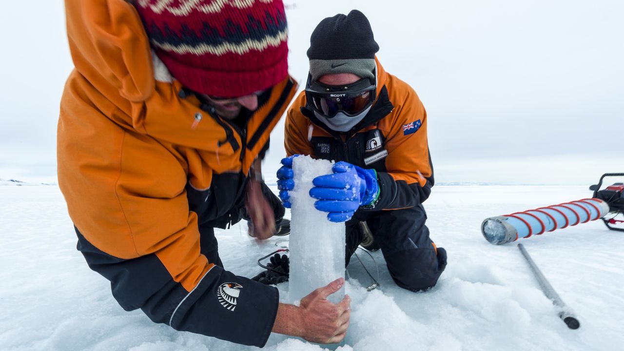 two researchers drill a core of ice in Antarctica