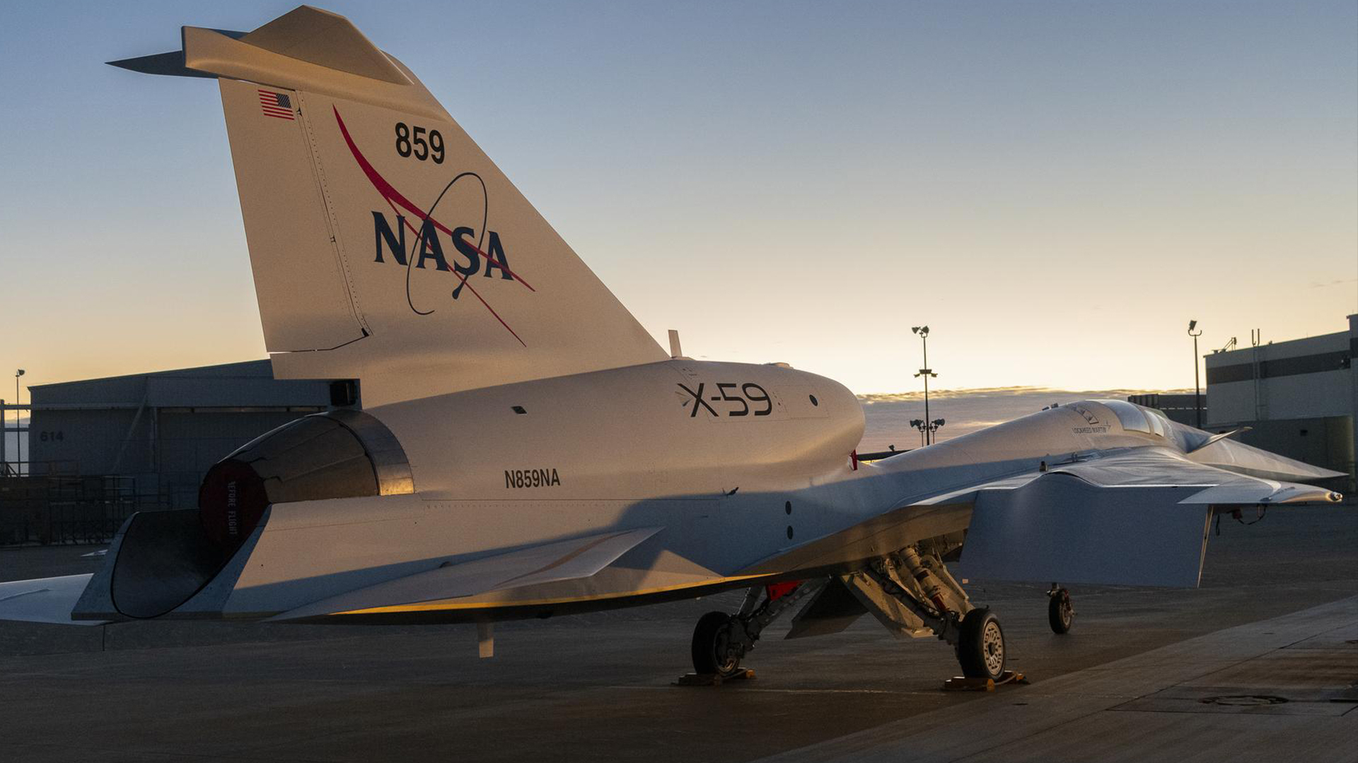 a rear view of an elongated blue-and-white jet with a colorful sunrise behind it