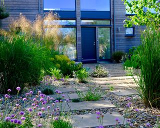 A front garden with shingle and paving stones leading up to a black front door