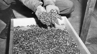Here we see at very a close up of two hands scooping up the contends of a large box filled with hundreds of wedding rings that the Nazis removed from their victims to salvage the gold.
