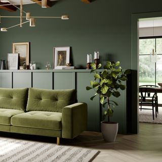 green living room with green sofa, paneling behind sofa, retro brass pendant, artwork behind sofa, rug, plant, dining room in background