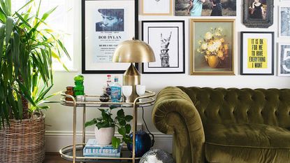 A selection of framed wall art decor in living room with olive green velvet sofa and brass bar cart drinks trolley decor