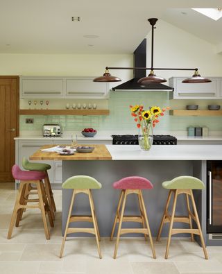 A pale green backsplash in a white kitchen with large island with pink and green bar stools