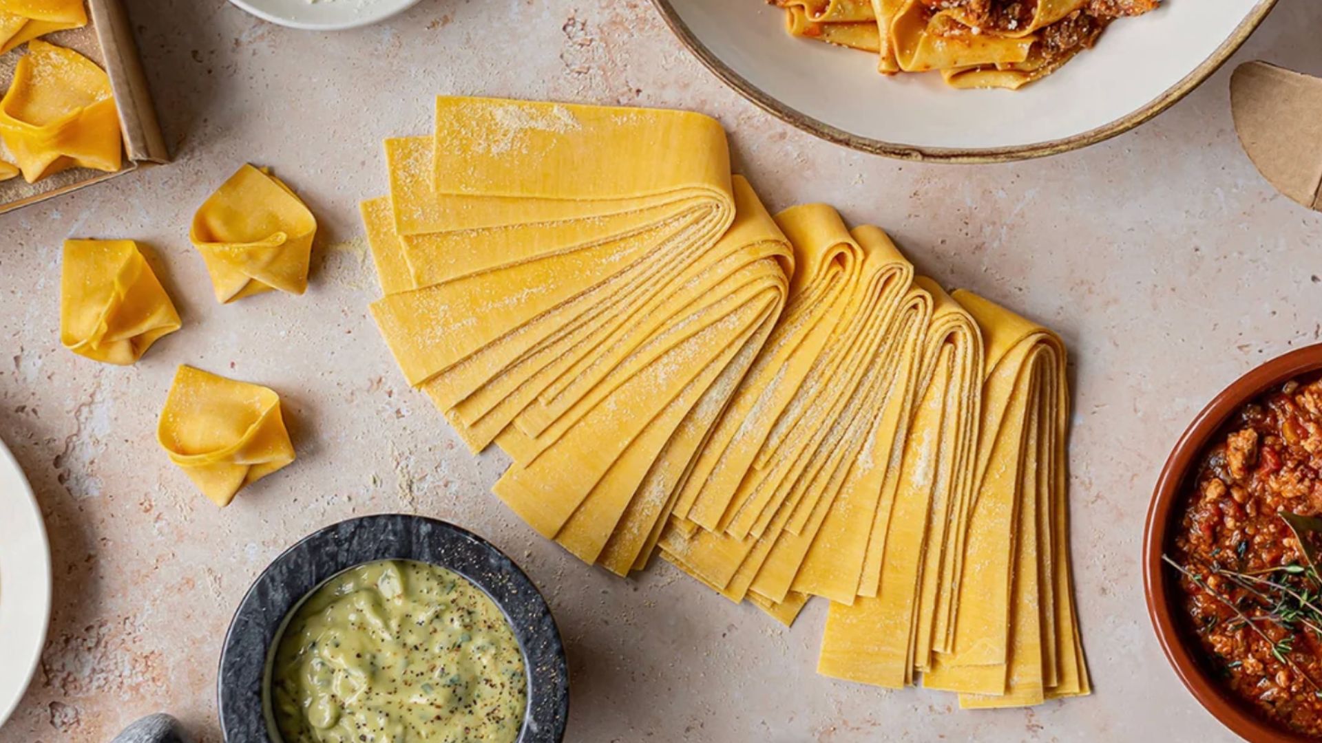 an image of some fresh pasta sheets laid out on a table with different sauces around it