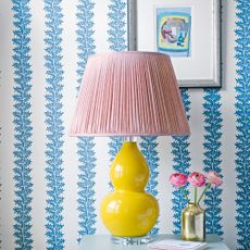 Blue and white patterned stripe wallpaper behind table with yellow and pink lamp