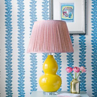 Blue and white patterned stripe wallpaper behind table with yellow and pink lamp