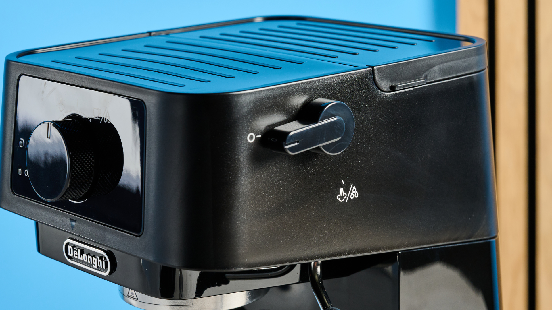 the de'longhi stilosa espresso machine in black, with one portafilter, a dial for espresso and milk steaming, and a plastic tamper, photographed against a blue background