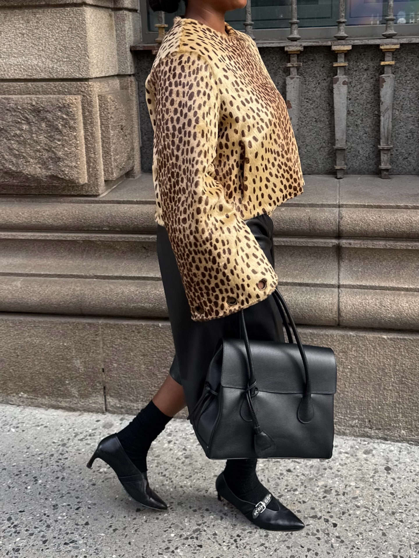 An image of an influencer wearing an autumn shoe trend, buckle heels, with a leopard jacket and black Bermuda shorts carrying a black leather tote