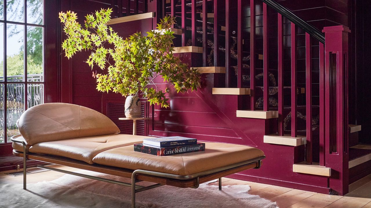 Entryway with glossy burgundy painted panelled walls and staircase, tan leather daybed and green foliage in clay pot