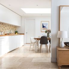 White kitchen with white cabinets and natural wooden counter with a wooden dining table and assorted chairs
