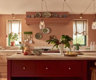 A pink kitchen with tongue and groove paneling on the walls, a dark pink kitchen island, and decorative plates hung on the walls