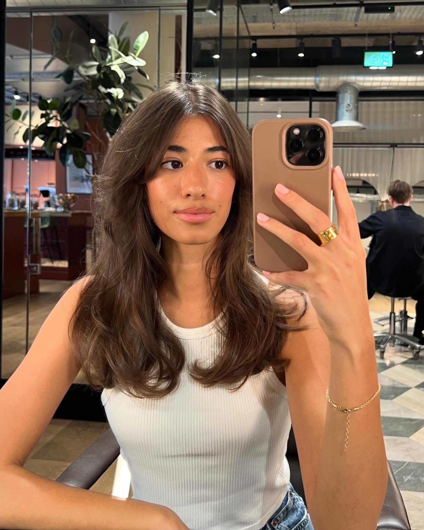 A woman taking a mirror selfie with a bouncy, layered haircut