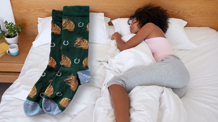 A woman lies asleep on the right side of the bed in side sleeping position (Getty). On the left side of the bed is a large pair of socks (Future)