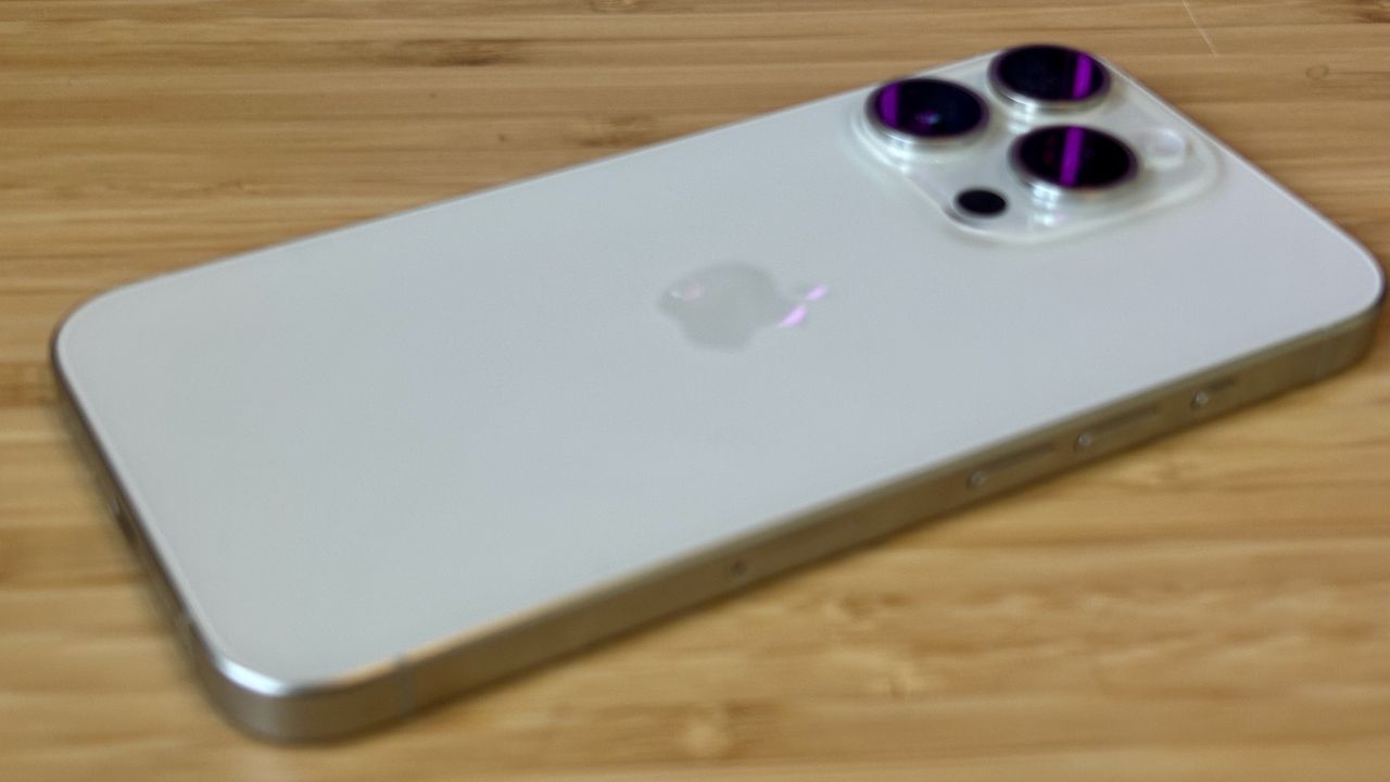 A grey titanium iPhone 15 Pro camera phone on a wooden desk