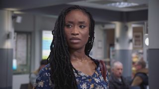 Ngozi dressed in a flowery navy top, looking deeply concerned before starting her shift at Holby ED.