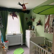 Nursery with green walls and curtains, white cot and zoo soft toys