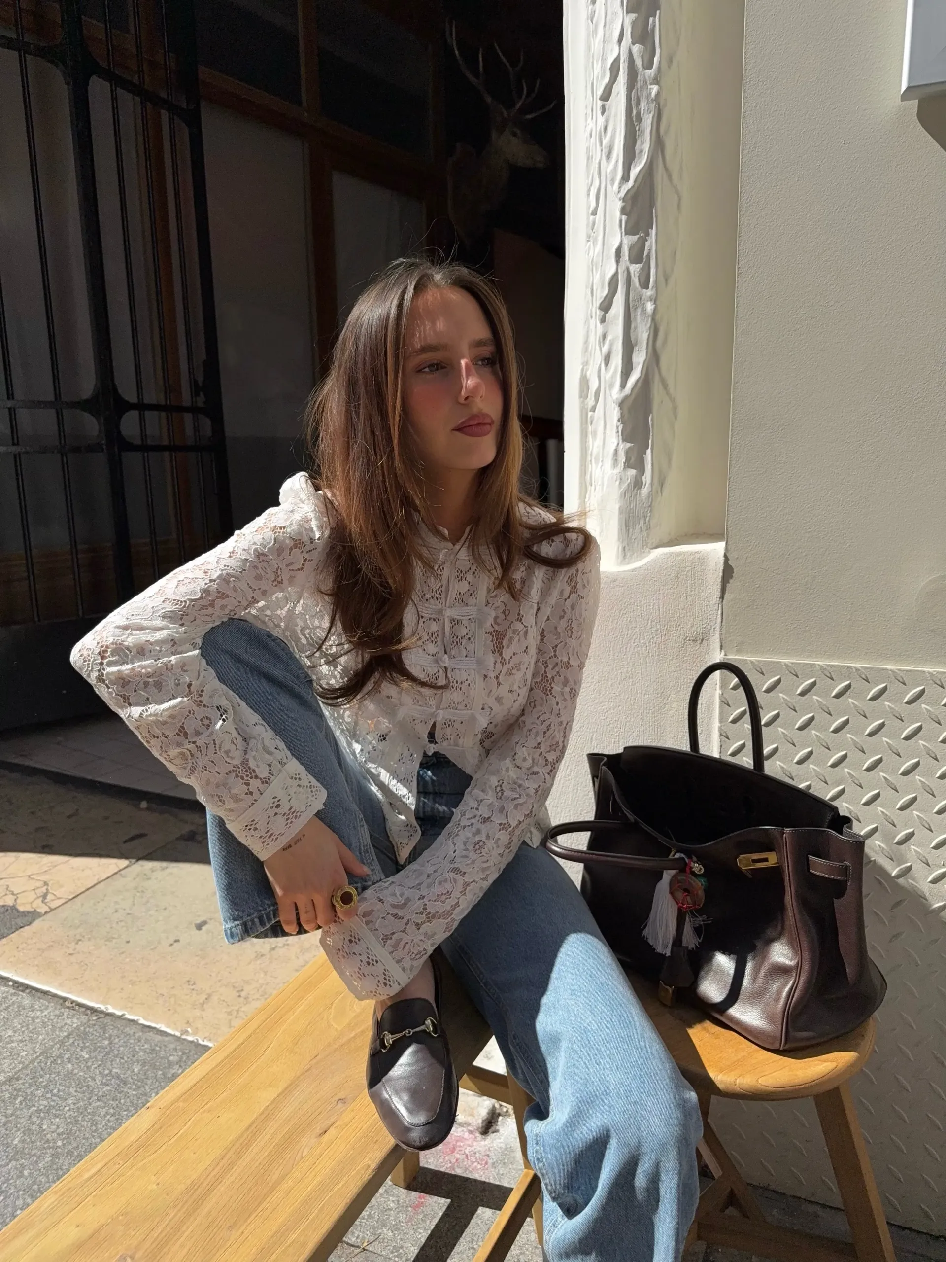 Woman sitting next to a warm brown handbag.