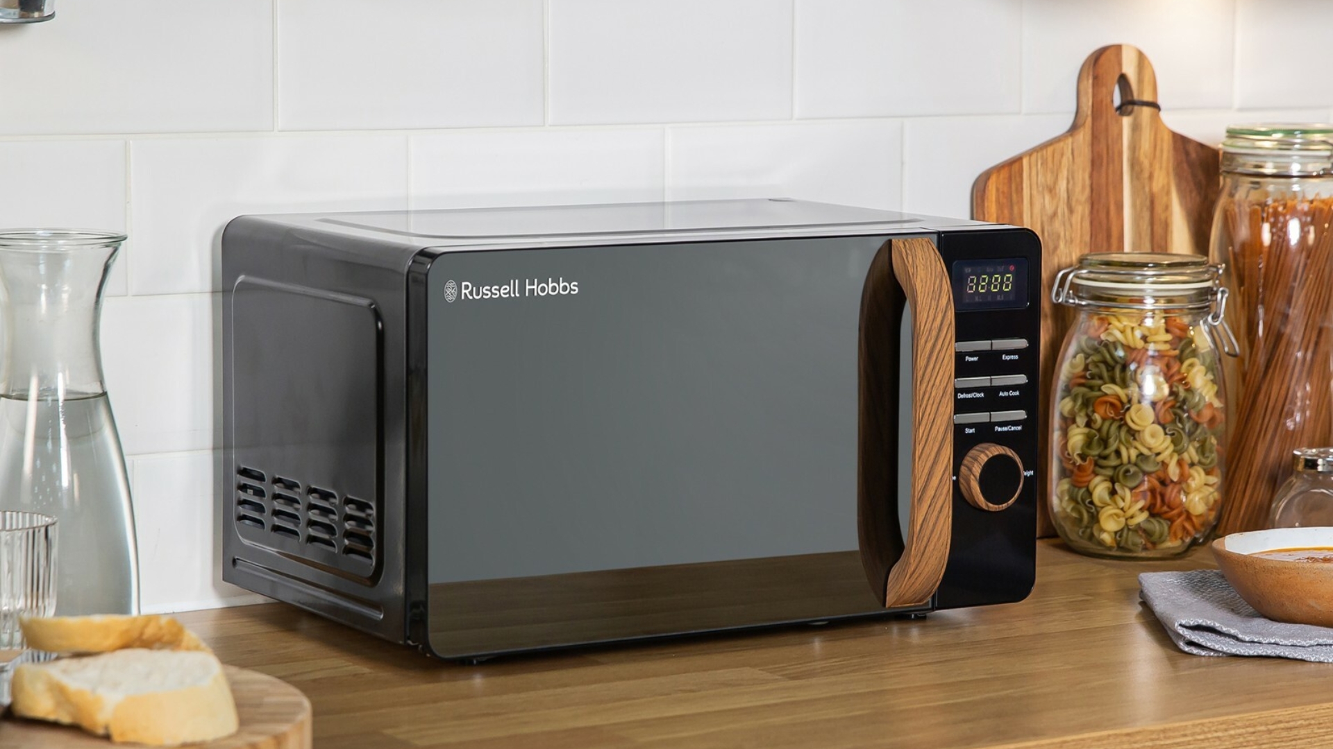 Russell Hobbs 17L Scandi Manual Microwave on a wooden counter with chopping boards and kilner jars around it