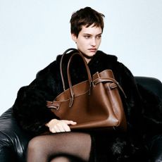 Woman wears faux fur coat and carries brown tote bag