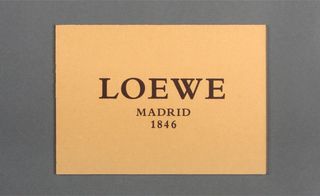 Front view of Loewe's peach invitation pictured against a grey background