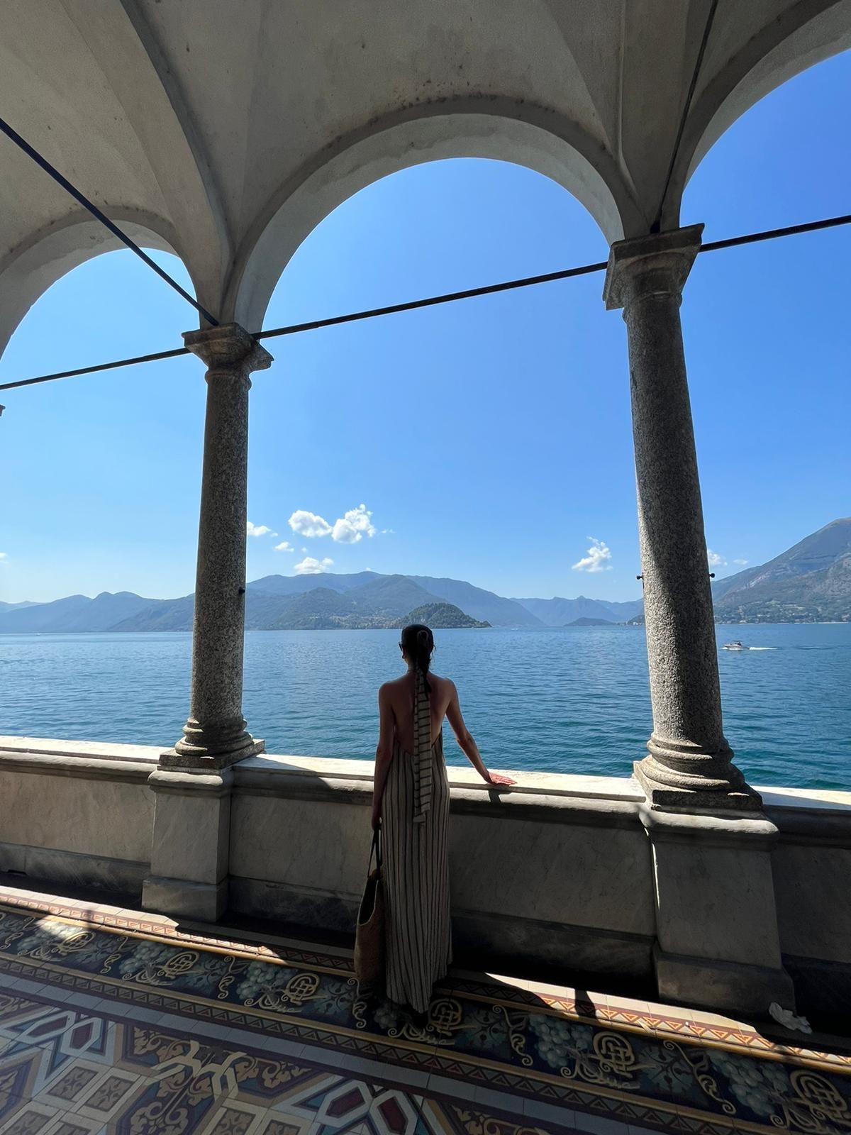 Woman standing on the lakeside of Lake Como underneath a marble arch