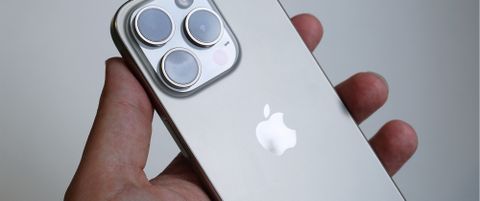 En mobiltelefon av typen iPhone 15 Pro holdes i en hånd.