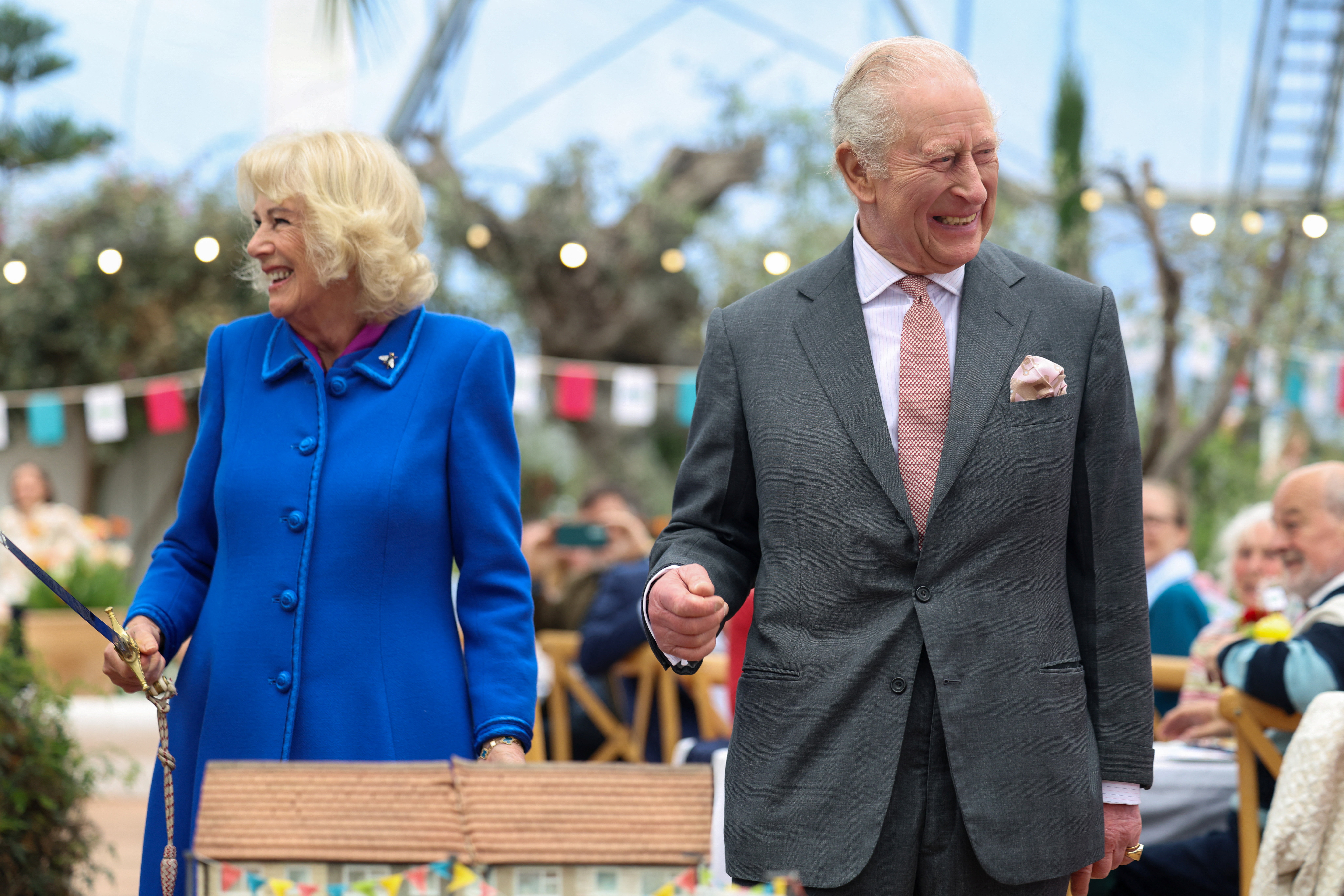 Queen Camilla holding a sword standing next to King Charles, laughing