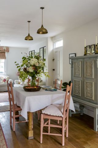 dining table and chairs with white tablecloth and green vintage dresser