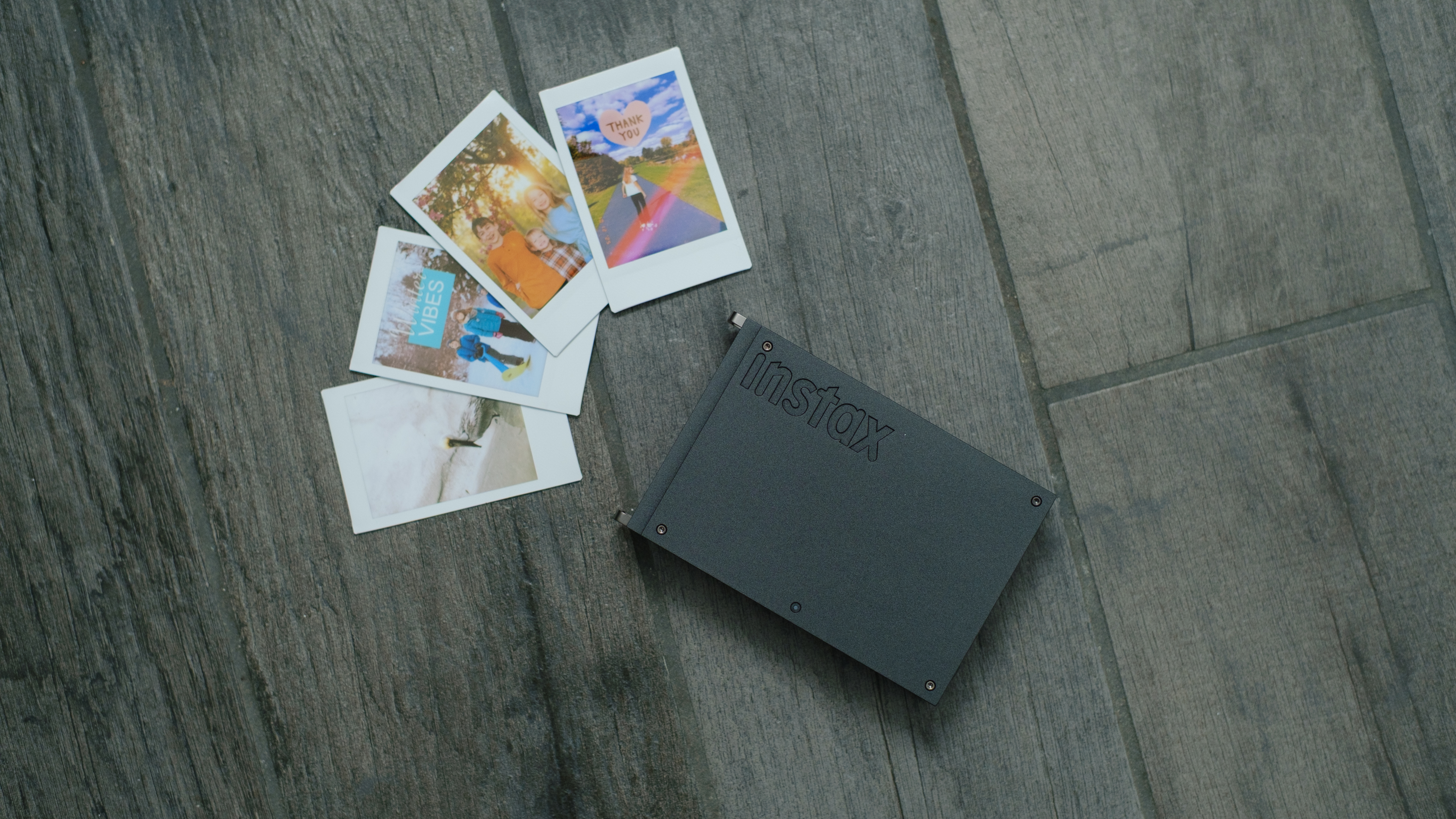 The Fujifilm Instax Mini Link+ on a gray background with instant prints