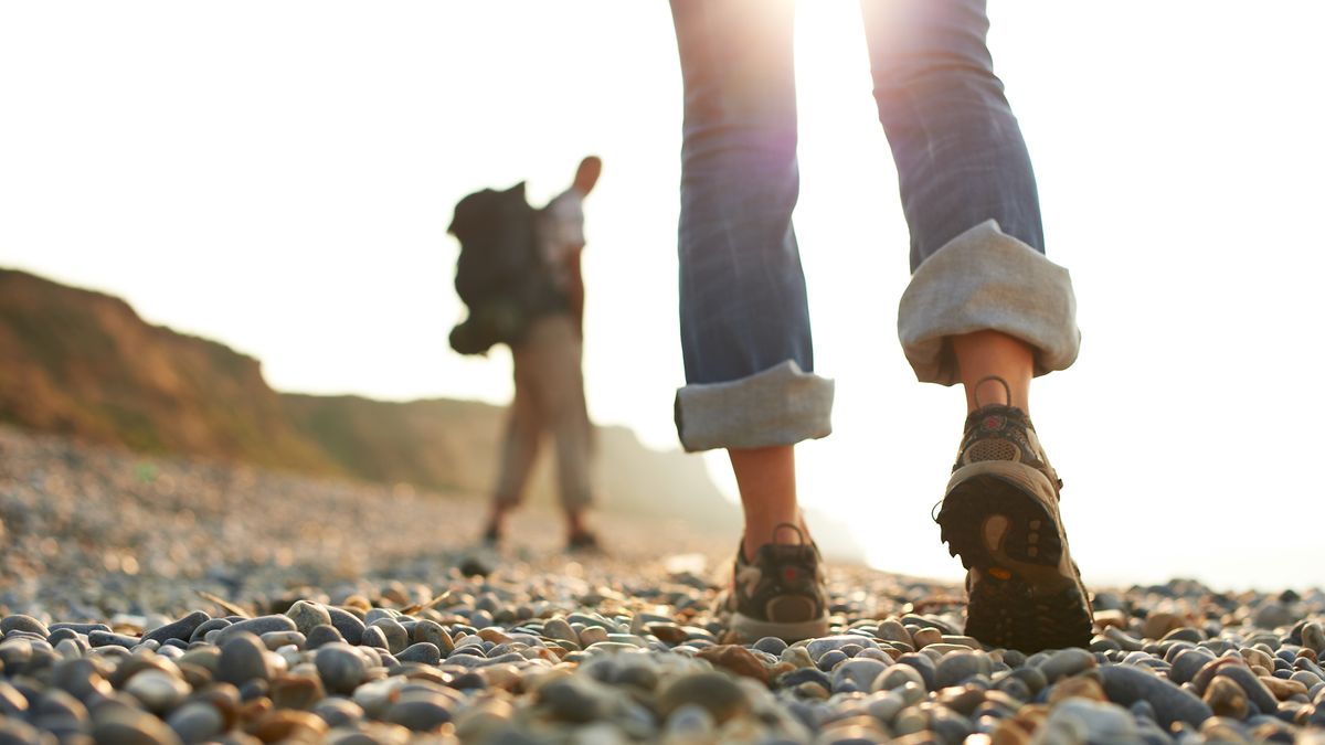 A close up of two people hiking on a pebble beach wearing jeans