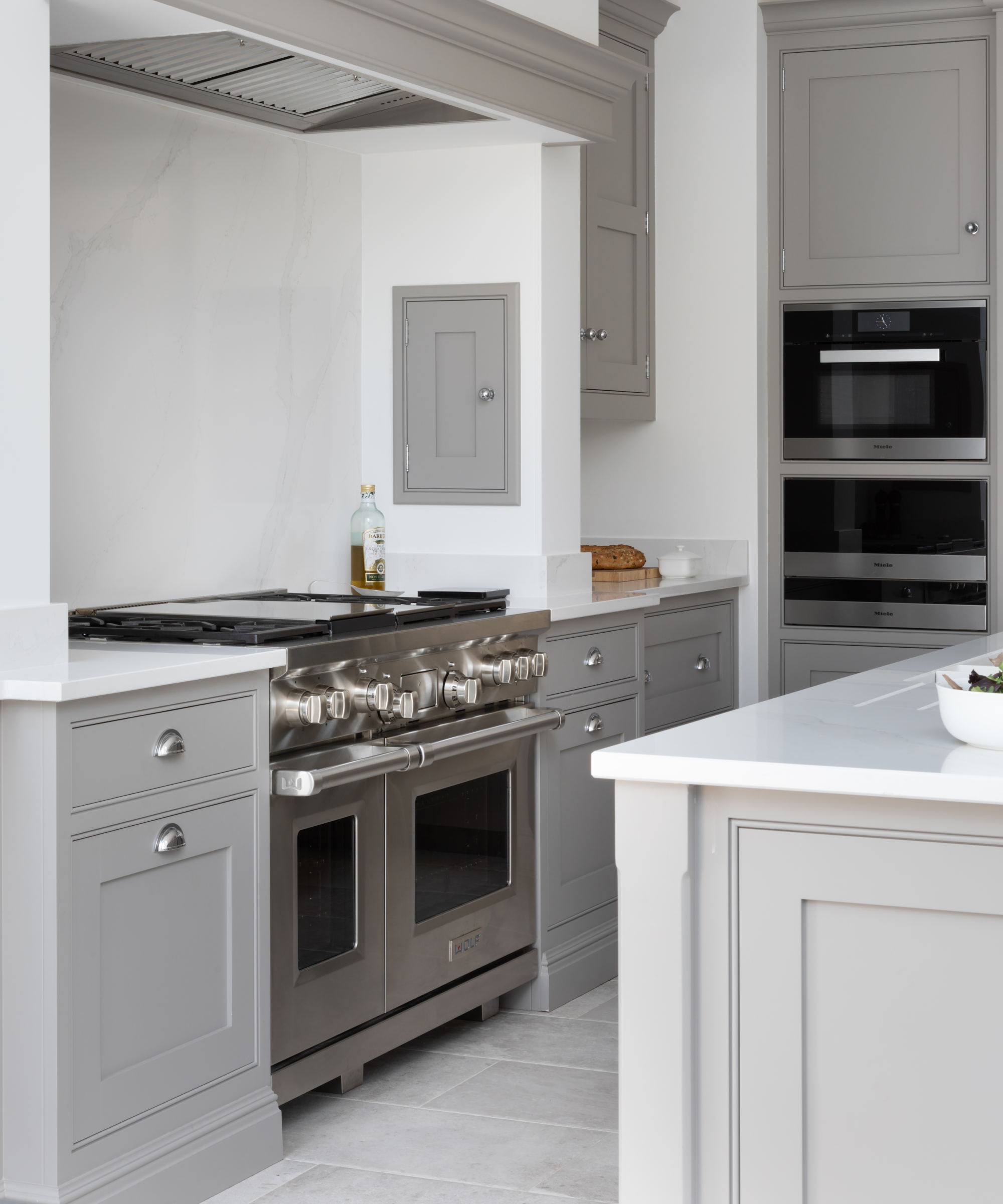 A kitchen with light gray cabinets and white walls and a large, built-in range cooker