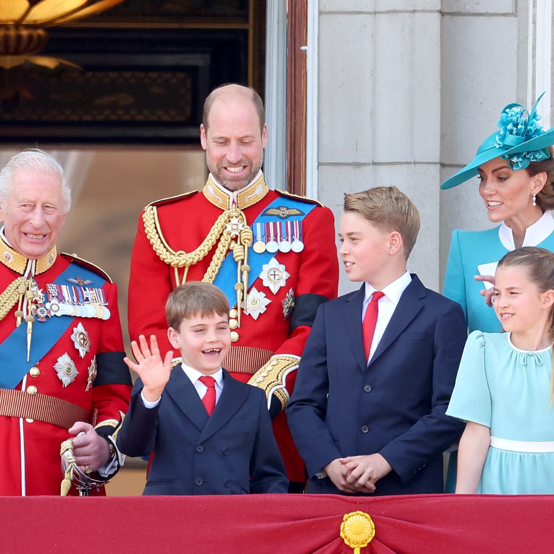King Charles and Prince William wear red military uniform, Prince Louis and Prince George wear navy suits with red ties, while Princess Kate and Prince Charlotte wear turquoise dresses on the Buckingham Palace balcony