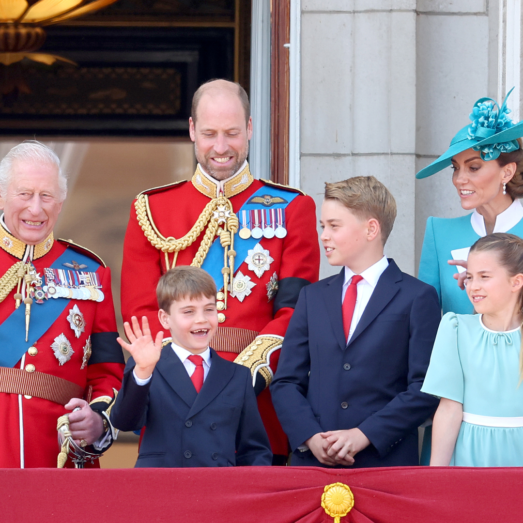 King Charles and Prince William wear red military uniform, Prince Louis and Prince George wear navy suits with red ties, while Princess Kate and Prince Charlotte wear turquoise dresses on the Buckingham Palace balcony