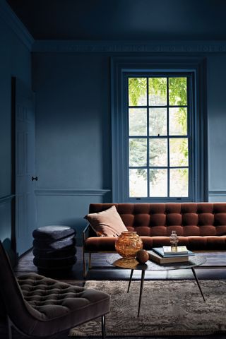 blue living room with brown couch, brown armchair, dark wooden floor, patterned rug, coffee table