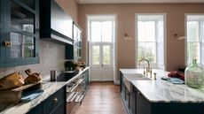 Large bright kitchen with dark blue cabinets, marble countertops, kitchen island, brass fixtures and bright floor to ceiling windows and doors to the back