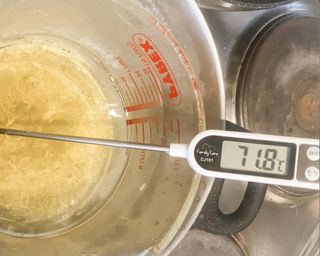 A food thermometer placed within a Pyrex glass measuring jug monitoring melted wax that has reached 71.8 celcius