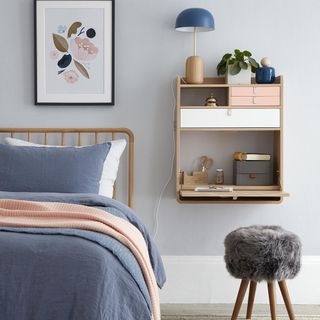 Blue bedroom with wall mounted side table and fluffy stool next to bed