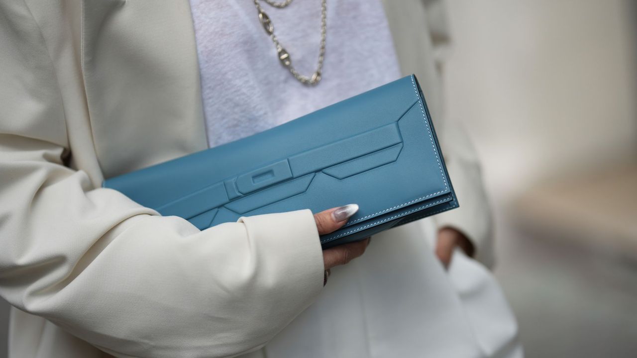 Woman wearing cat eye nails holding an Hermes clutch bag