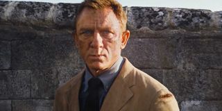 James Bond stands in front of a stone and looks sad in No Time To Die