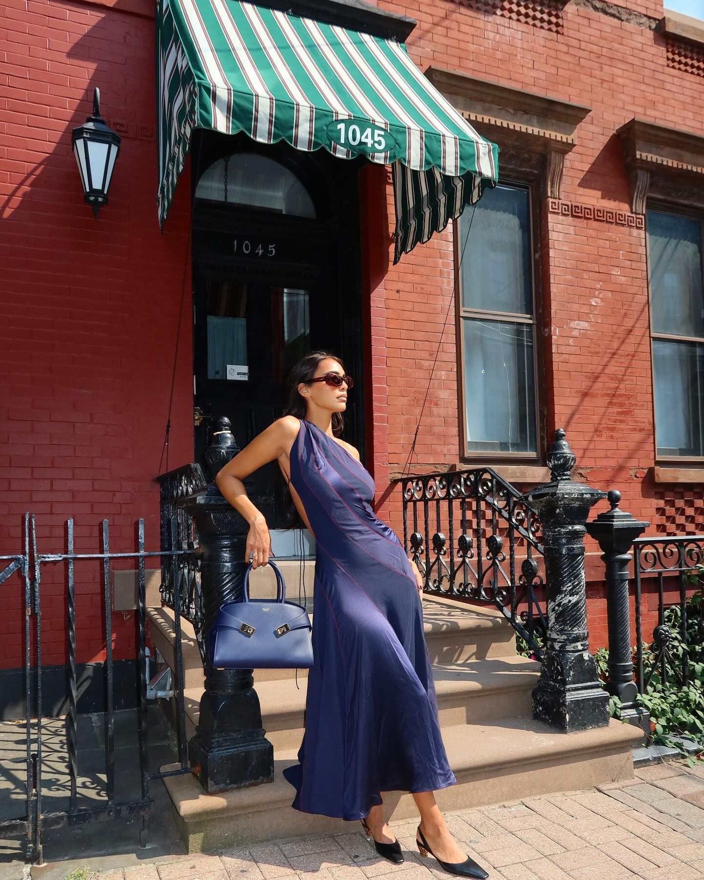 Influencer @sandrashehab stands outside in the sun holding a Ferragamo bag and wearing a navy dress.