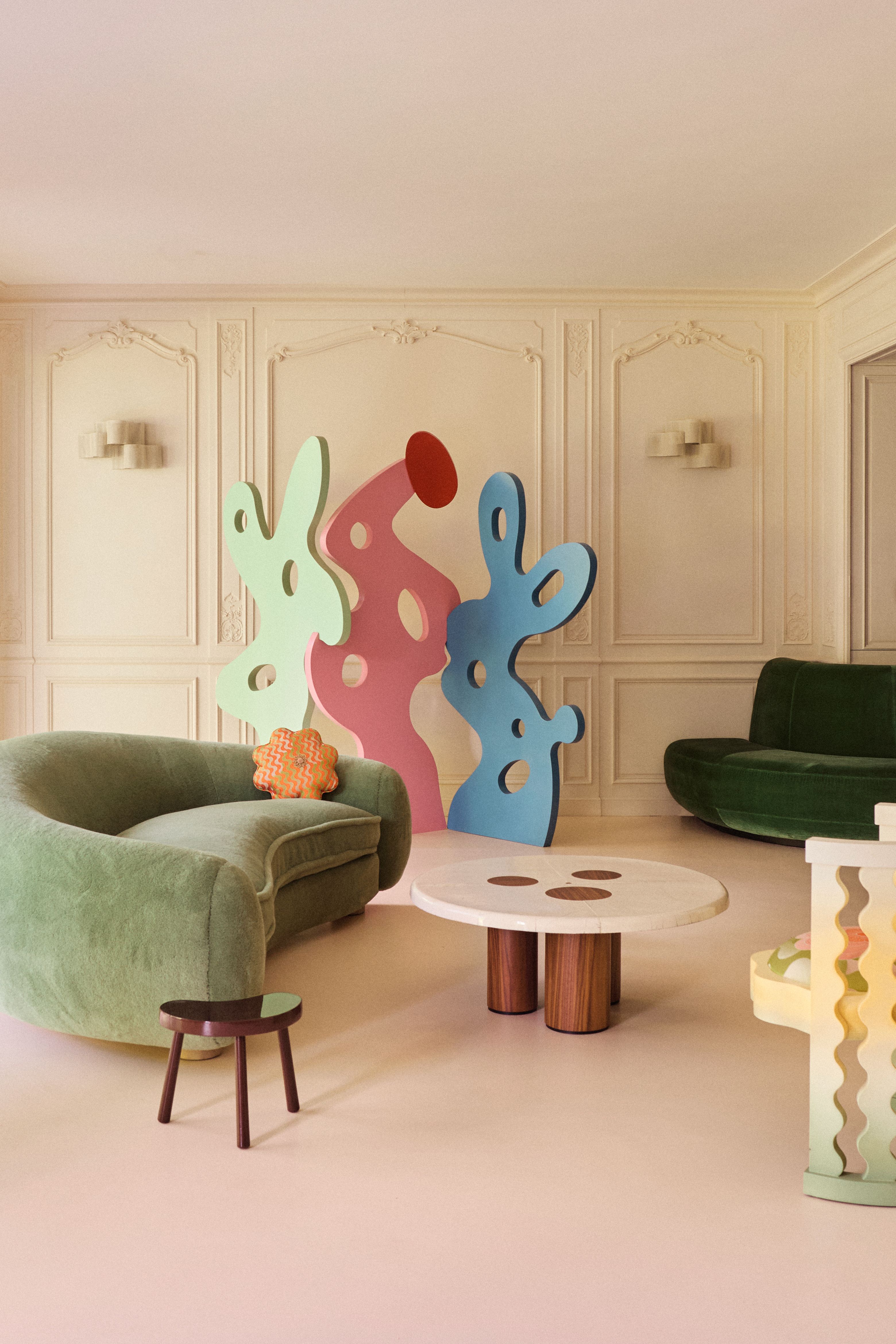 a modern beige living room with green sofas and 2d cut out sculptures