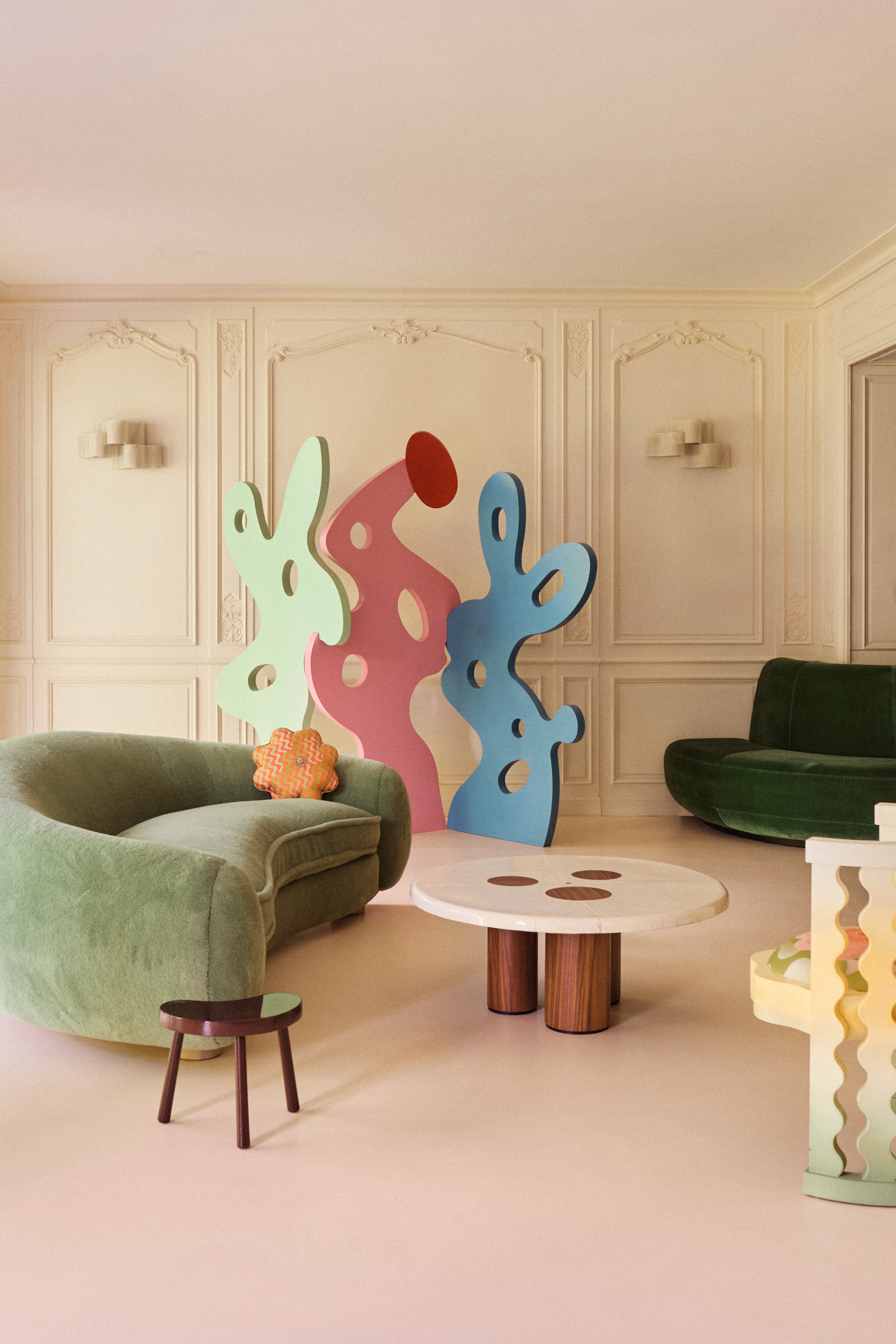 a modern beige living room with green sofas and 2d cut out sculptures