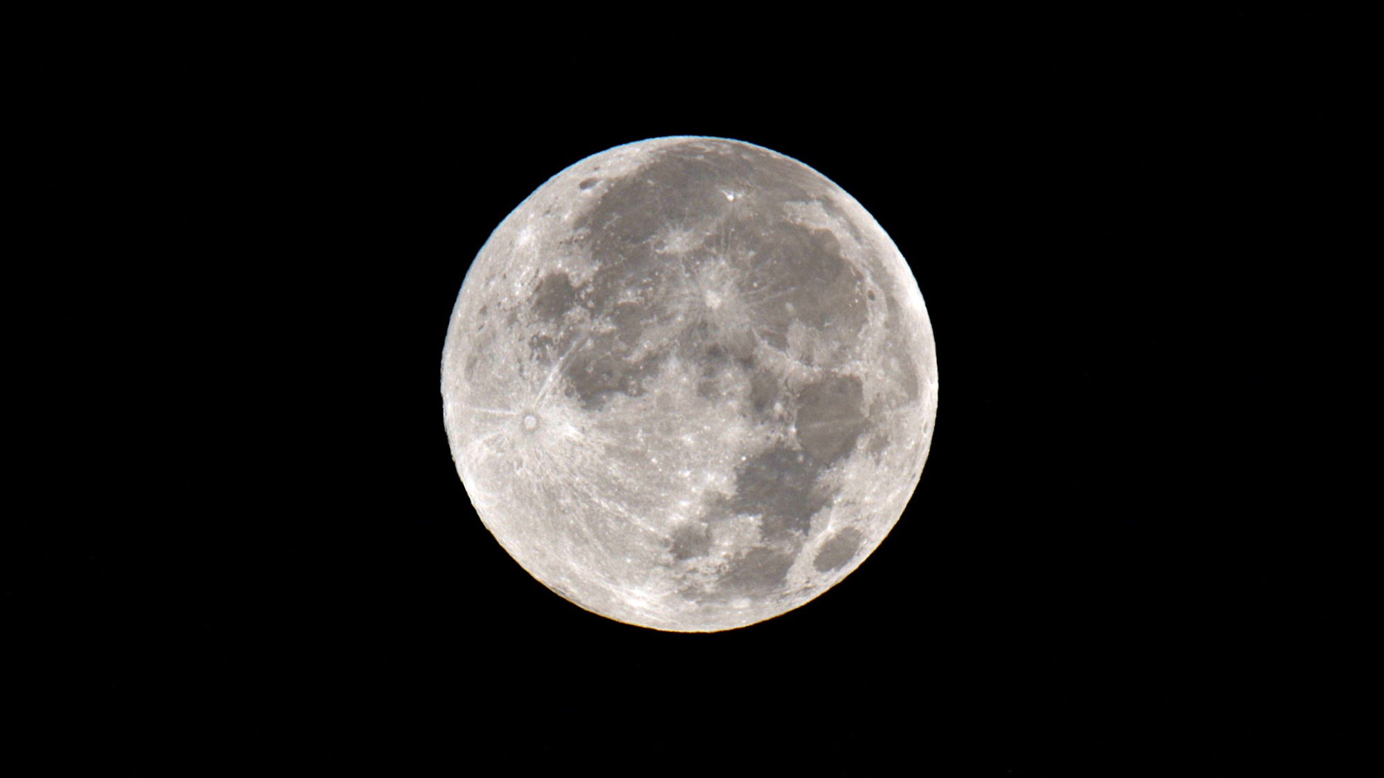 A silver full moon shines in a black sky.