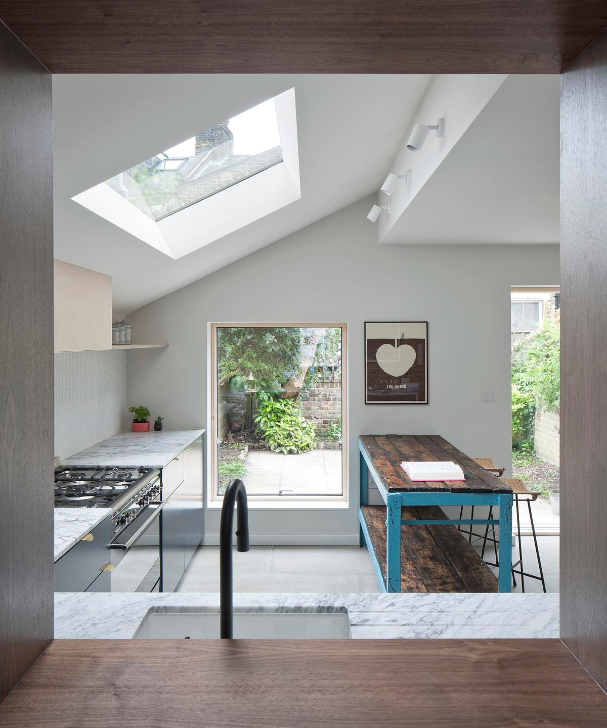 window style opening with deep walnut reveal looking into kitchen extension with sloped ceiling, rooflight and large picture window looking onto garden with deep oak reveal
