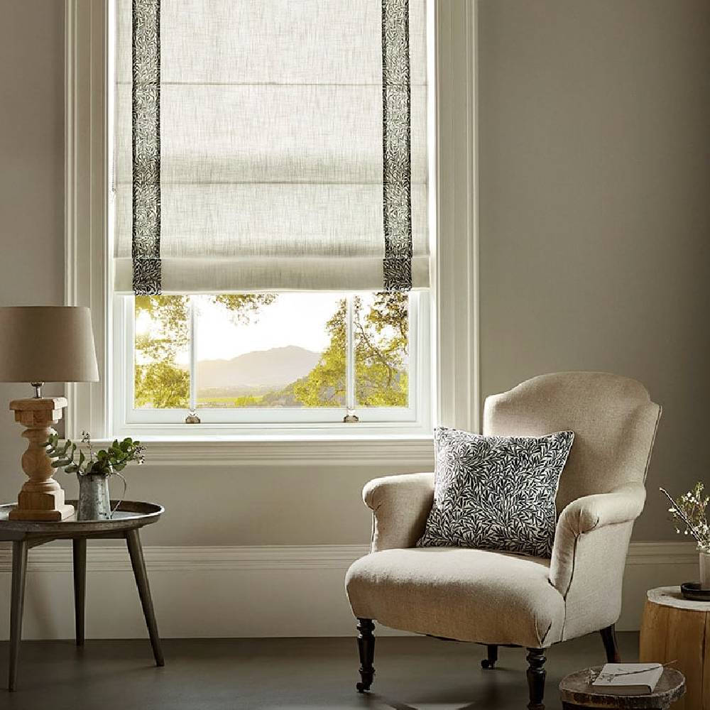 A modern lounge window view, with a cream armchair, and a matching cream and navy blind from Blinds2go.