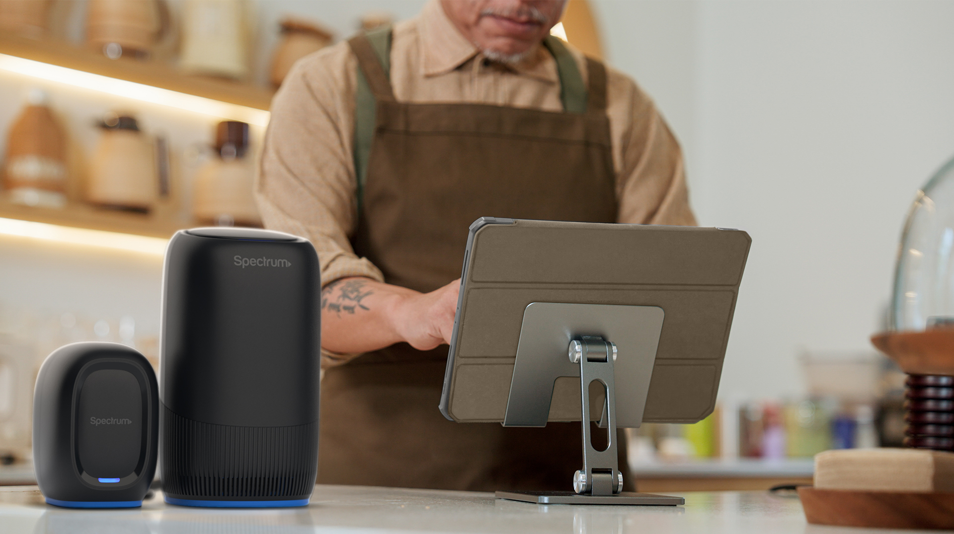 A man stands behind a counter in an apron with a Spectrum Invincible Router sitting on the counter to the right.