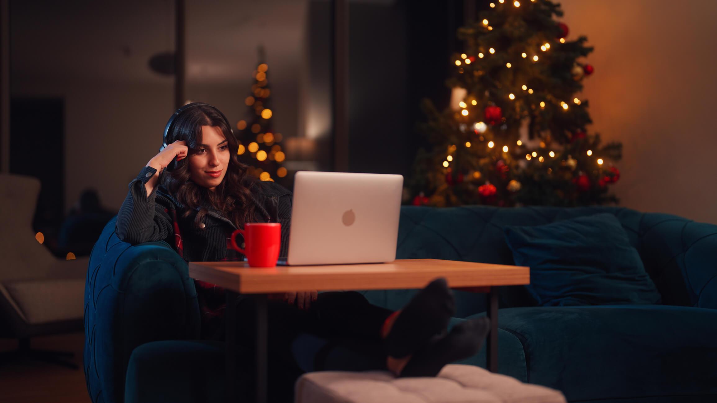  A young woman is relaxing at home and using her laptop in the living room during Christmas 